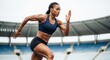 © Николай Срибяник - A determined female athlete sprints on a stadium track, showcasing strength and speed, with a blurred stadium in the background.