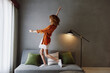 © SHOTPRIME STUDIO - Cheerful young woman in a stylish orange shirt and white skirt dancing joyfully in a modern lounge with a minimalist background