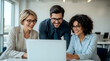 © Ada - Laptop, collaboration and business people in the office while working on a company project. Technology, joyful group of three diverse professionals gathered around a laptop in a bright, modern office
