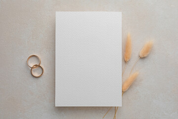 Wall Mural - Wedding invitation card, golden rings and spikelets on color textured table, flat lay