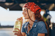 © SHOTPRIME STUDIO - lifestyle woman in modern boho-western denim street style enjoying a refreshing drink, smiling with eyes closed, film color tones creating warm vibes outdoors