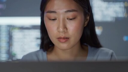 Close up of an asian woman looking at a computer screen with code in the background