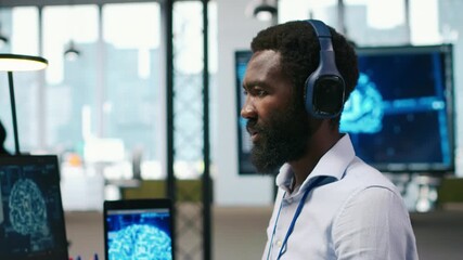 Poster - Computer scientist in office integrating AI machine learning systems to streamline workflows, earing headphones. African american man uses artificial intelligence on devices, listening music, camera A