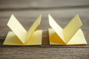 Aufkleber - Two yellow paper origami shapes with symmetrical folds placed side by side on wooden table, creating minimalistic and creative composition