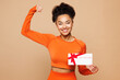 © ViDi Studio - Young strong fitness trainer instructor sporty woman wears orange clothes spend time in home gym hold store gift coupon voucher card isolated on plain beige background. Workout sport fit abs concept.
