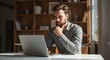 © PrabuanaAndika - Thoughtful Young Man Working on Laptop in Sunlit Home Office, Concentrated on Project, Business Professional, Remote Work, Home Workspace