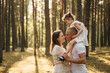 © aleonovs - A joyous child on father's shoulders, her mother is nearby looking up, all smiling in a sun-drenched pine forest