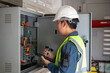 © JD Studio - Engineer performs fire safety inspection on electrical distribution board wearing safety helmet and reflective vest while using tablet for accurate data recording