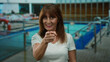 © Krakenimages.com - Senior hispanic woman smiling and pointing while standing at a resort pool area, enjoying a relaxed outdoor atmosphere on holiday.