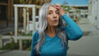 © Krakenimages.com - Senior woman with grey hair standing outdoors on a street, wearing a blue sweater, depicting an expressive moment amidst urban surroundings on a sunny day.