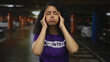 © Krakenimages.com - Woman expressing frustration in a dimly lit parking garage, wearing a purple volunteer shirt, surrounded by blurred cars, capturing a moment of stress in an urban setting.