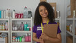 © Krakenimages.com - Young woman volunteering at a charity center smiles warmly while holding a clipboard, standing amidst shelves of donation items in an indoor room.