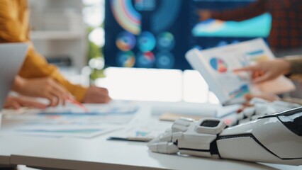 Poster - A collaborative workplace showcases a robot hand alongside charts and graphs during a team strategy meeting, highlighting innovation and technology in business.Noogenesis