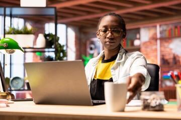 Poster - Woman in home office drinking coffee in the morning and browsing internet, researching information. African american teleworker starting job shift with hot beverage, preparing to do work tasks