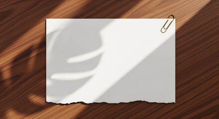 Poster - Blank paper with torn edge held by paperclip on wooden table with leaf shadow