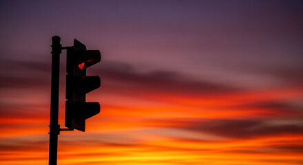 Poster - Traffic light with red signal against a vibrant sunset sky