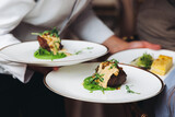 Waiter in uniform serving dishes on party event, server carrying plates with food at the table, catering service on wedding reception, cafe restaurant table service, waiters arranging dinner banquet