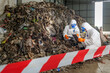© BESTIMAGE - Workers in protective suits and masks inspecting large pile of waste and debris inside industrial recycling or waste processing facility with safety barrier