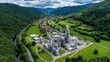 © M - Industry Amidst Verdant Hills: An aerial view of a large industrial complex nestled in a valley, showcasing the contrast between technology and the natural environment.