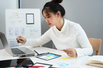 Fototapete - Website designer, Creative planning phone app development template layout framework wireframe design, User experience concept, Young asian UX designer working on smartphone application at office.