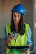 © Ljustina - Female engineer using smartphone and holding clipboard on construction site