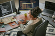 © Seventyfour - Young adult Black woman working at desk using desktop computer with code on monitors, typing on keyboard, surrounded by notepad, smartphone, apple, and laptop in modern office