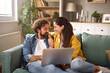© Stockphotodirectors - Two people share a joyful moment on a sofa, focused on a laptop. The warm lighting and inviting decor create a comfortable atmosphere for their activities.
