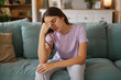 © Stockphotodirectors - Teenage girl appears troubled while sitting on a vibrant couch in a cozy living room, reflecting on her feelings and the difficulties of growing up.