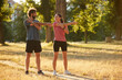 © Stockphotodirectors - Two individuals perform dynamic stretching exercises in a sunlit park, promoting health and wellness through physical activity and engagement in nature.