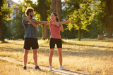 Two individuals perform dynamic stretching exercises in a sunlit park, promoting health and wellness through physical activity and engagement in nature.