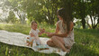 © Vikulya - Mother with little daughter sitting on blanket in park and playing with toys. Soft focus