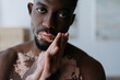 © Bliss - Portrait of shirtless african american man with vitiligo looking at camera at home