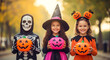 © Syam - Three smiling children in Halloween costumes holding jack-o'-lantern buckets.