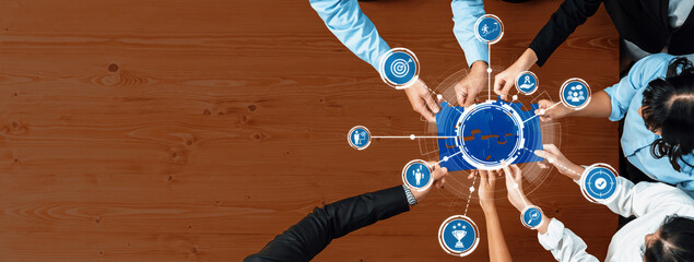 Poster - A top-down view of a diverse team collaborating over a wooden table, surrounded by conceptual icons. This image represents strategic discussions and innovative solutions in business. Amity