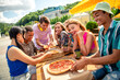 © deagreez - Group of friends enjoying pizza and coffee outdoors on a sunny day while bonding and celebrating the relaxed atmosphere
