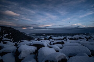 Wall Mural - Snow-covered rocks by the sea at dusk.