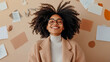 © sommersby - Joyful woman with natural Afro hair and eyeglasses, eyes closed in pure happiness on a calm surface with scattered papers, concept of creative bliss or relaxation.