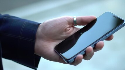 Poster - Close Up Hand Holding Blue Smartphone With Silver Ring and Blue Blazer Sleek Design Mobile Technology Urban Background