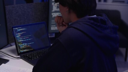 Asian programmer developer student diligently writing code problem solving on multiple screens at dark home office workstation