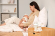 © Pixel-Shot - Bottle of milk with toy on table against woman breastfeeding her baby in bedroom, closeup