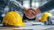 © CStock - Two business professionals shaking hands in a construction office, conveying partnership and cooperation.