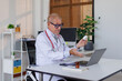 © David - Serious old mature professional male doctor using laptop computer in hospital office video call medical webinar training, writing healthcare report, consulting patient online at telemedicine meeting.