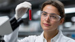 © Ali Hamza Tullah - High-resolution close-up of female lab assistant in white coat and safety goggles examining blood sample in test tube inside sterile hospital laboratory with modern diagnostic equipment.