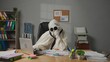 © kinomaster - Halloween businessman ghost in white sheet sits at office desk works on laptop, tired bored expression, sighing and thinking. Happy halloween business concept.