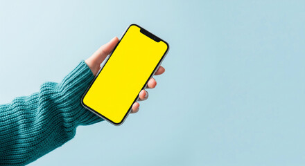 Aufkleber - Hand in teal sweater holds phone with blank yellow screen against light-blue background Mockup for app presentation or advertisement