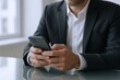 © Generative AI - Businessman in formal suit using smartphone at modern office desk during workday.