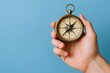 © Generative AI - Hand holding a vintage brass compass against a smooth blue background detailed close-up shot.