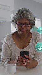 Poster - Animation of connected icons forming globes, senior african american woman using laptop in kitchen