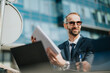© qunica.com - A professional man in a suit holding documents and discussing work outside an office building.