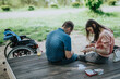 © qunica.com - A couple sits on a wooden platform near nature surroundings, engaging in a card game together, fostering connection and spending quality time outdoors.